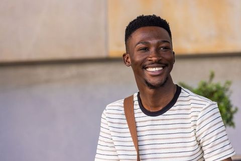 Smiling african man wearing striped tee and crossbody bag in urban outdoor portrait