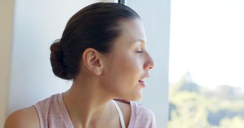 Serene woman closing eyes by bright window in minimalist interior, calm profile portrait