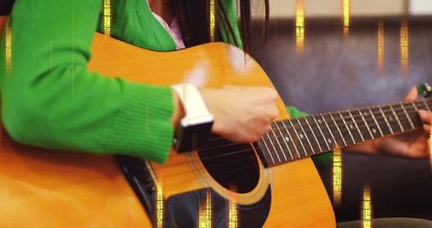 Playing asian woman in green sweater strumming acoustic guitar while wearing smartwatch