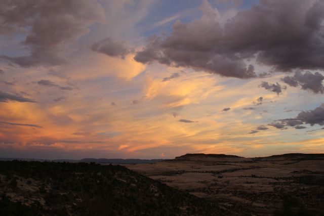 This mesmerizing scene highlights the beauty of a desert landscape at sunset. The sky is painted with shades of orange, pink, and purple as the sun sets, casting a dramatic and serene atmosphere over the rolling hills and distant mountains. Ideal for use in travel magazines, nature blogs, and as a backdrop for relaxation or inspirational quotes.