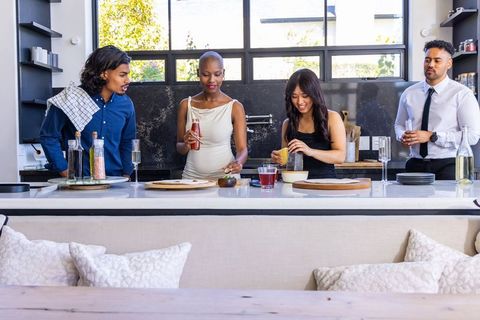 Diverse friends preparing cocktails and squeezing citrus at modern sunlit kitchen island