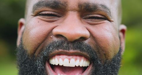 Joyful bearded man laughing in park with greenery