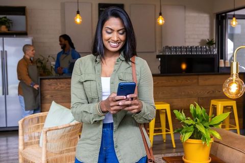 Indian woman smiling while using smartphone in cozy modern cafe with staff in background