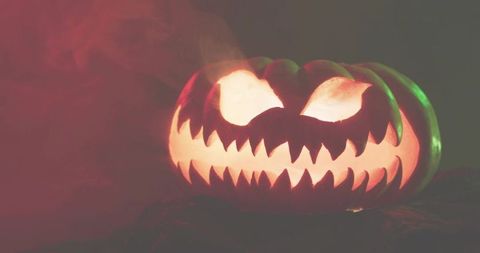 Glowing carved jack-o'-lantern with jagged grin, green rim light and drifting smoke for halloween