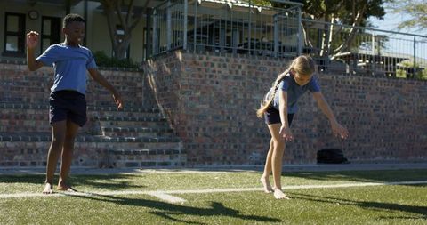 Children balancing on turf line in sunny schoolyard barefoot teamwork and playful exercise