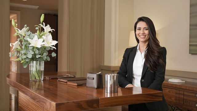 Smiling receptionist in black blazer welcoming guests at modern wooden reception desk