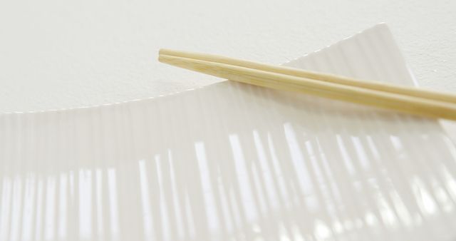 A pair of wooden chopsticks rests on a white, ribbed ceramic plate, with copy space. The simplicity of the scene suggests a minimalist or Asian-inspired aesthetic.