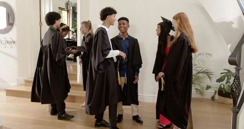 Diverse Graduates Celebrating and Exchanging Diploma Covers in Elegant Foyer