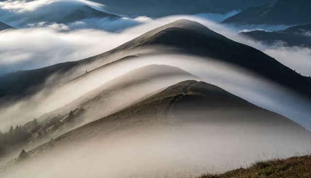 Ethereal Mist Flowing Over Grassy Mountain Ridges With Soft Morning Light Creating Valleys