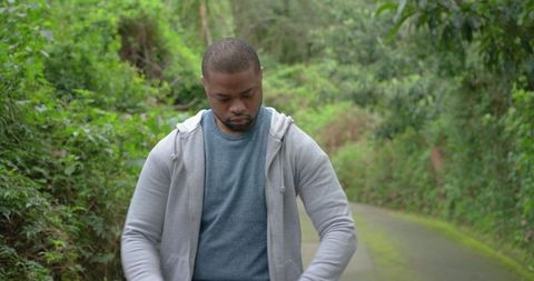 African american man adjusting gray hoodie on mossy woodland lane, overcast outdoor