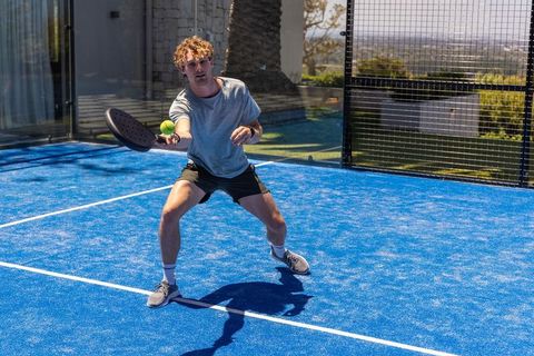 Competitive padel player lunging to return neon ball on vibrant blue outdoor court