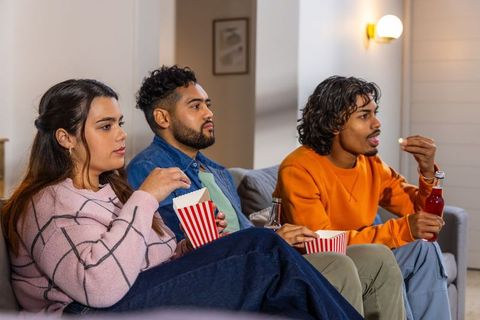 Friends watching movie on couch eating popcorn and drinking soda at cozy home night