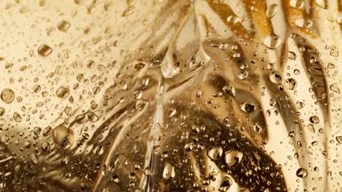 Golden Water Droplets Rolling and Forming Central Rivulet on Glass Macro Video