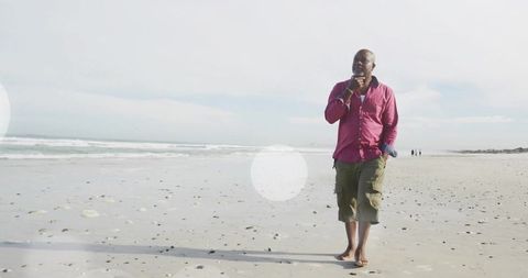 Senior Man in Magenta Shirt Walking Barefoot on Tranquil Beach