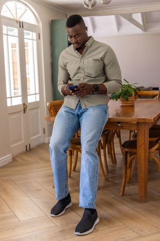African american man sitting on dining table checking smartphone in minimalist interior