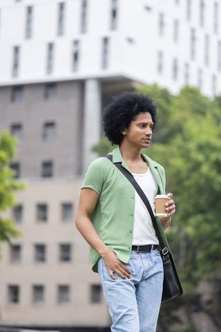 African man walking with coffee and messenger bag in modern city streetscape urban commute