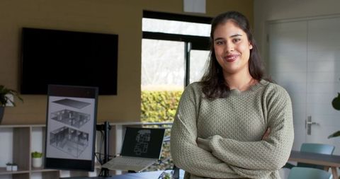 Smiling woman standing with arms crossed in architect studio wearing sage knit sweater