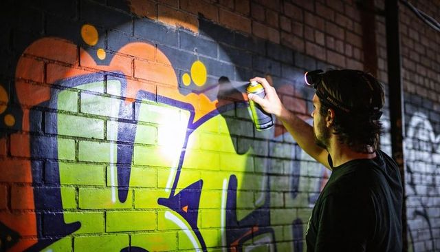 Urban artist spraying vibrant neon graffiti on brick wall at night with headlamp spraycan
