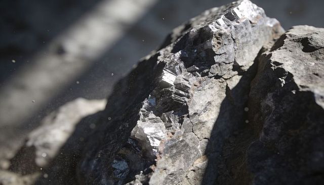 Sunlit silvery mineral vein glinting in fractured rock close-up, metallic crystal detail