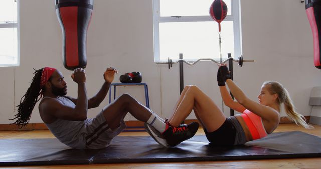 An African American male fitness trainer is guiding a Caucasian female client through an abdominal workout in a gym, with copy space. They are focused on their exercise routine, demonstrating a commitment to health and fitness.
