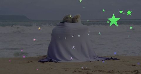 Couple cuddling under blanket on beach with starry overlay