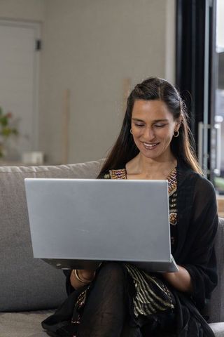Indian woman working from home on laptop wearing embroidered tunic and gold bangles