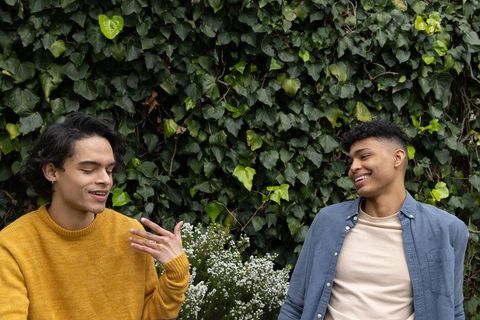 Young men chatting and laughing in garden with ivy wall and white flower blooms