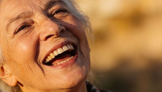 Laughing senior woman embracing golden hour light close-up with warm bokeh