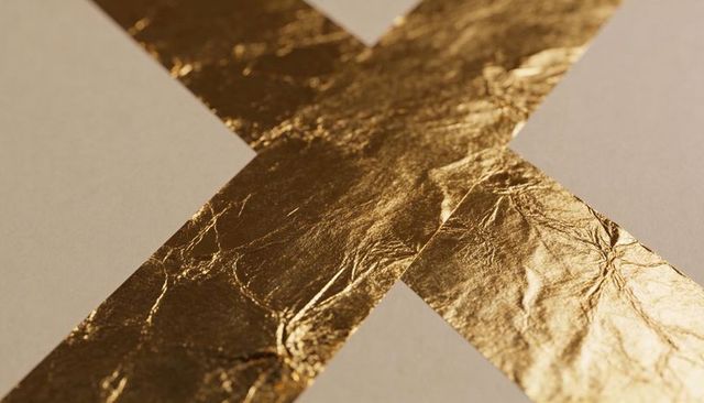 Crossed gold foil strips on beige paper macro texture for luxury background and design