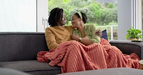 African American Couple Cuddling on Sofa Under Coral Throw Blanket in Bright Living Room