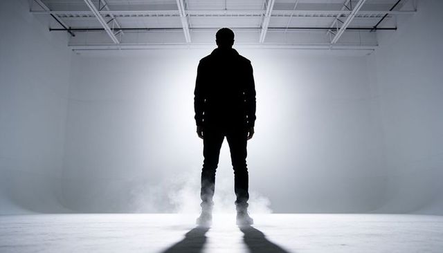 Backlit silhouette standing in fog-filled studio with dramatic halo and long shadow