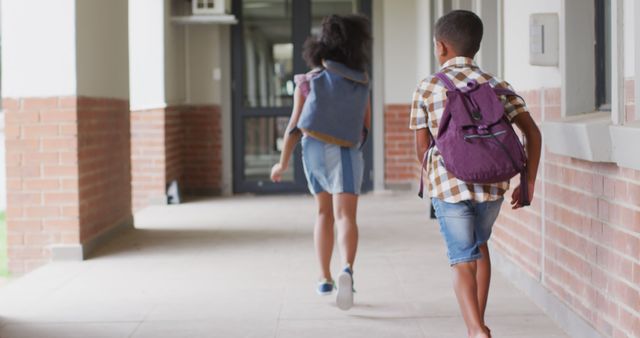 Children are seen running through a school corridor with backpacks, indicating excitement and enthusiasm. Ideal for use in educational materials, back-to-school campaigns, or advertisements for school supplies and children's clothing. It captures the kinetic energy and joy of young students in a school environment.