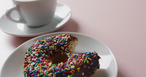 Close-Up of Donut with Sprinkles and Coffee Cup on Pink Background