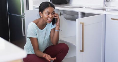 Worried woman calling for plumbing help in kitchen
