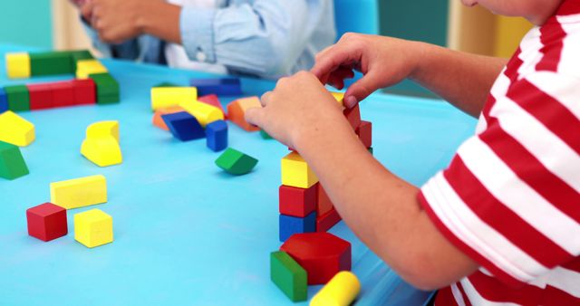Children's hands are engaging with colorful building blocks at a table. This scene highlights creativity, education, and skill development. Ideal for concepts of early education, preschool activities, learning through play, and fostering mental skills in children. Can be used in educational materials, promotional content for child learning centers, and parenting blogs.