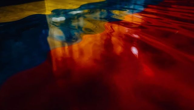 Rippling glossy pigment waves blending red blue yellow orange in iridescent gradient