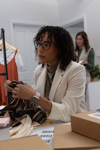 Diverse female entrepreneurs sorting and packing striped garments at boutique workspace