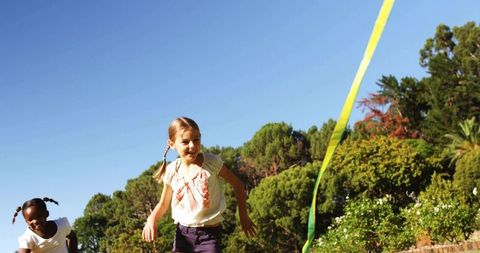 Young girls running with ribbon on sunny lawn enjoying outdoor play and summer fun