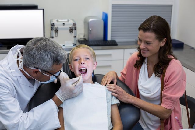 Dentist examining young patient with dental tool while mother watches. Ideal for illustrating pediatric dental care, family health, and supportive healthcare environments. Useful for medical websites, dental clinic promotions, and educational materials on oral health.