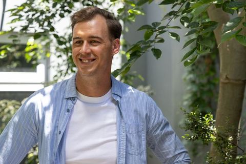 Smiling dressed man standing in sunlit courtyard wearing white tee and striped shirt