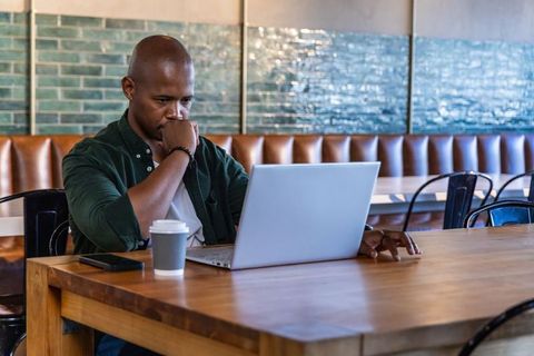 African american man working on laptop in modern cafe with coffee and focused expression