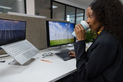 African american professional sipping mug while typing with solar and wind displays