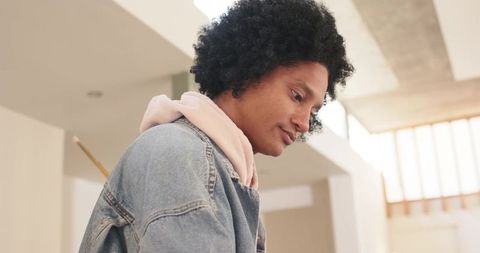 Contemplative black man leaning forward in minimal gallery wearing denim jacket and hoodie