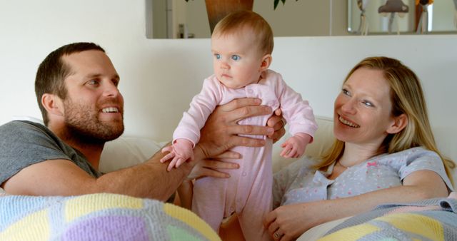 Front view of mid adult caucasian parents playing and holding baby on bed in a comfortable home - Download Free Stock Photos Pikwizard.com