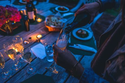 Elegant Evening Champagne Pouring at Candlelit Outdoor Dinner on Rustic Wooden Table