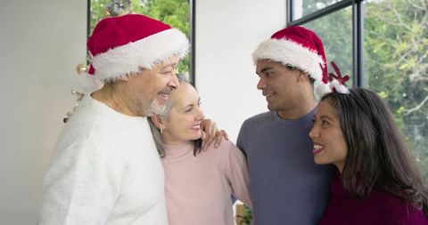 Multigenerational diverse family celebrating Christmas wearing Santa hats in modern living room