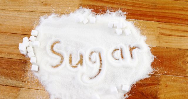 Granulated sugar is spread out on a wooden surface, with the word Sugar written in it, surrounded by sugar cubes, with copy space. Highlighting the concept of sugar consumption, this image can be used in discussions about diet, nutrition, and health.