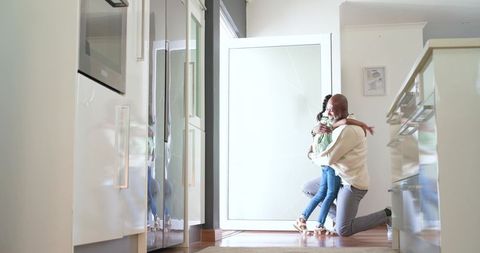African american father kneeling and hugging child in bright modern foyer with warm sunlight