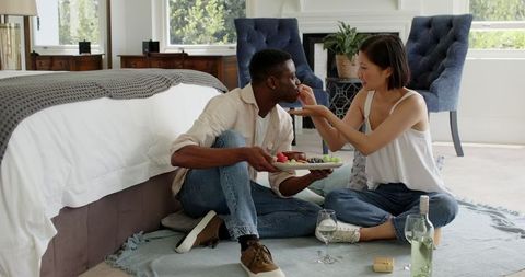 Romantic couple enjoying wine and fruit in cozy bedroom setting
