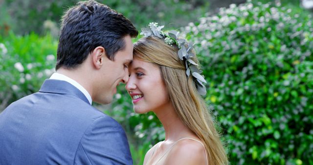 A young Caucasian couple shares an intimate moment, with the woman wearing a floral headpiece and the man in a suit, with copy space. Their close proximity and affectionate expressions suggest a romantic relationship, celebrating an engagement or wedding.